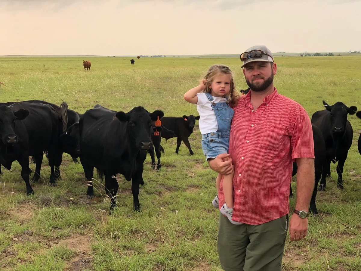 Josh holding his daughter in the pasture with their cattle